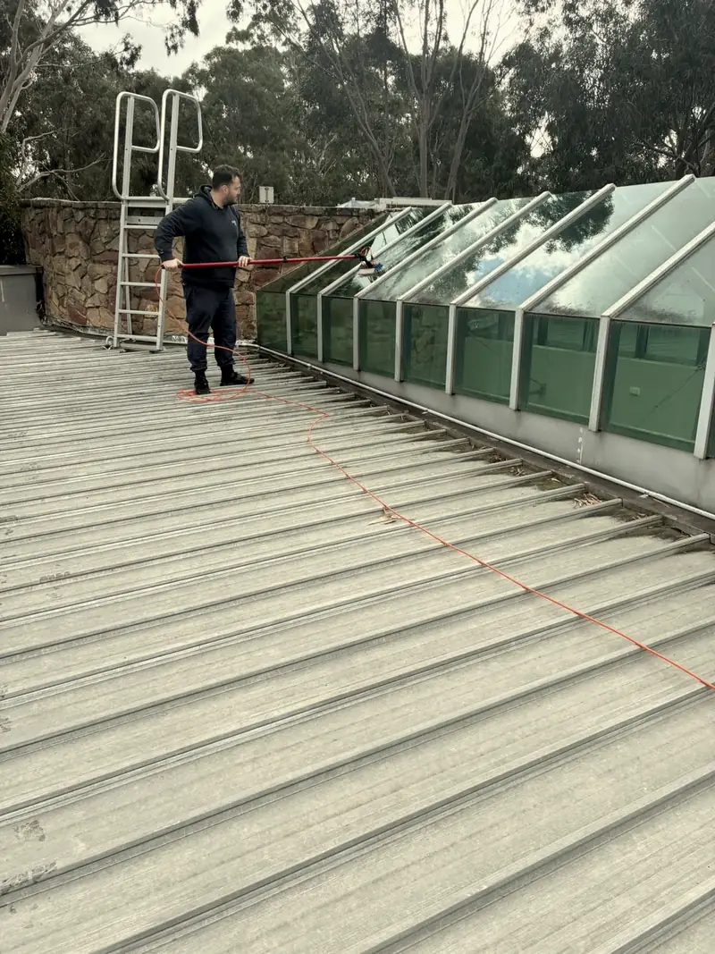 A technician cleaning a row of rooftop skylights from a metal roof