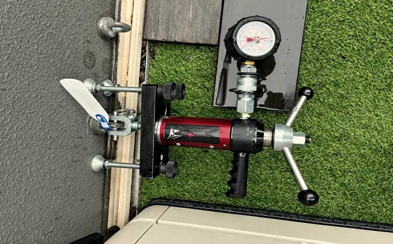 A hydraulic anchor pull-tester with pressure gauge clamped to a roof eyebolt anchor during certification testing